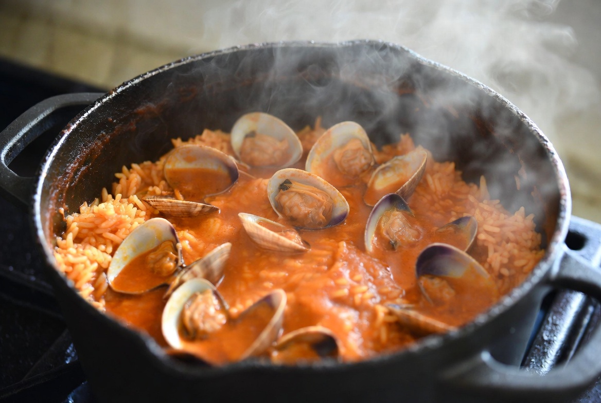Arroz con zamburi&ntilde;as coci&eacute;ndose en cazuela, con almejas en la superficie &ndash; etapa clave de la receta