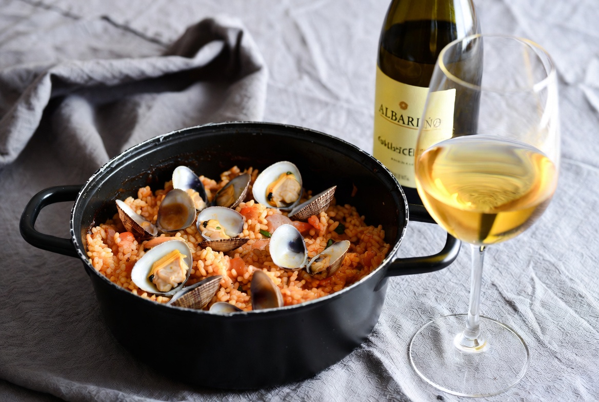 Plato terminado de arroz con zamburi&ntilde;as servido con una copa de vino Albari&ntilde;o &ndash; combinaci&oacute;n perfecta