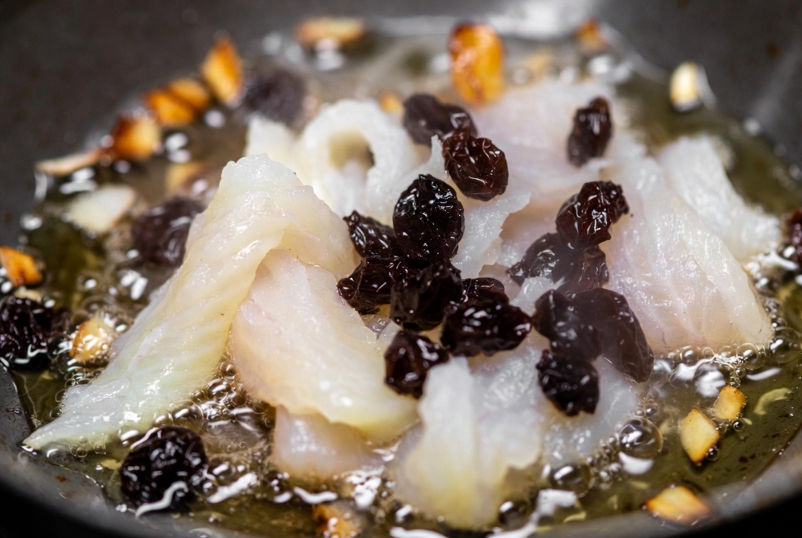 Bacalao desalado y pasas salte&aacute;ndose en aceite de oliva para un revuelto tradicional.