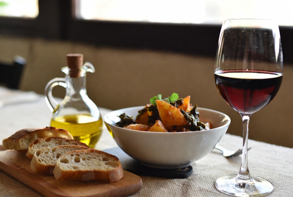 Plato de borrajas con patatas servido en la mesa con pan, vino y aceite de oliva.