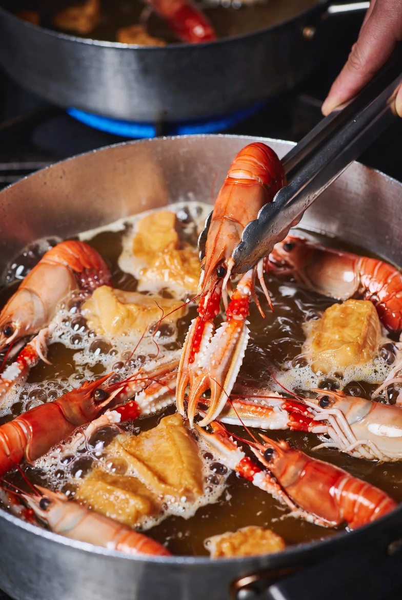 Trozos de langosta y pescado siendo sellados en aceite para una caldereta