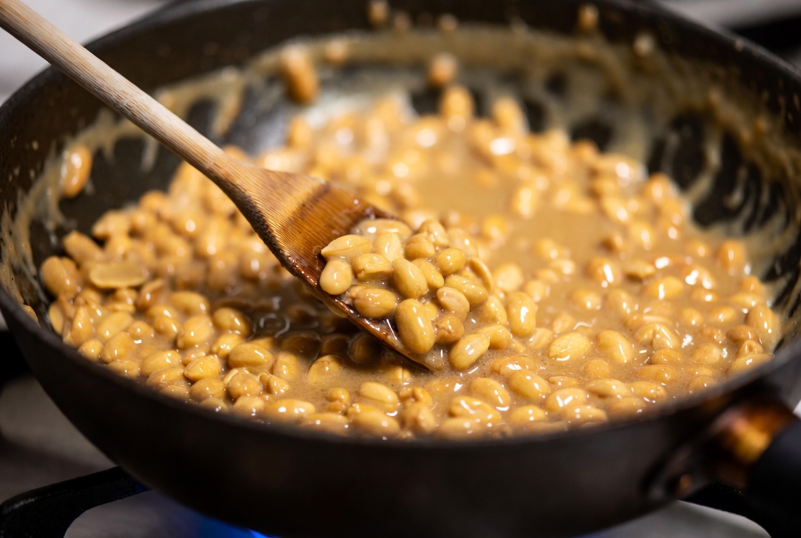 Man&iacute;es en un cazo siendo cubiertos por caramelo l&iacute;quido dorado durante la preparaci&oacute;n de garrapi&ntilde;adas.