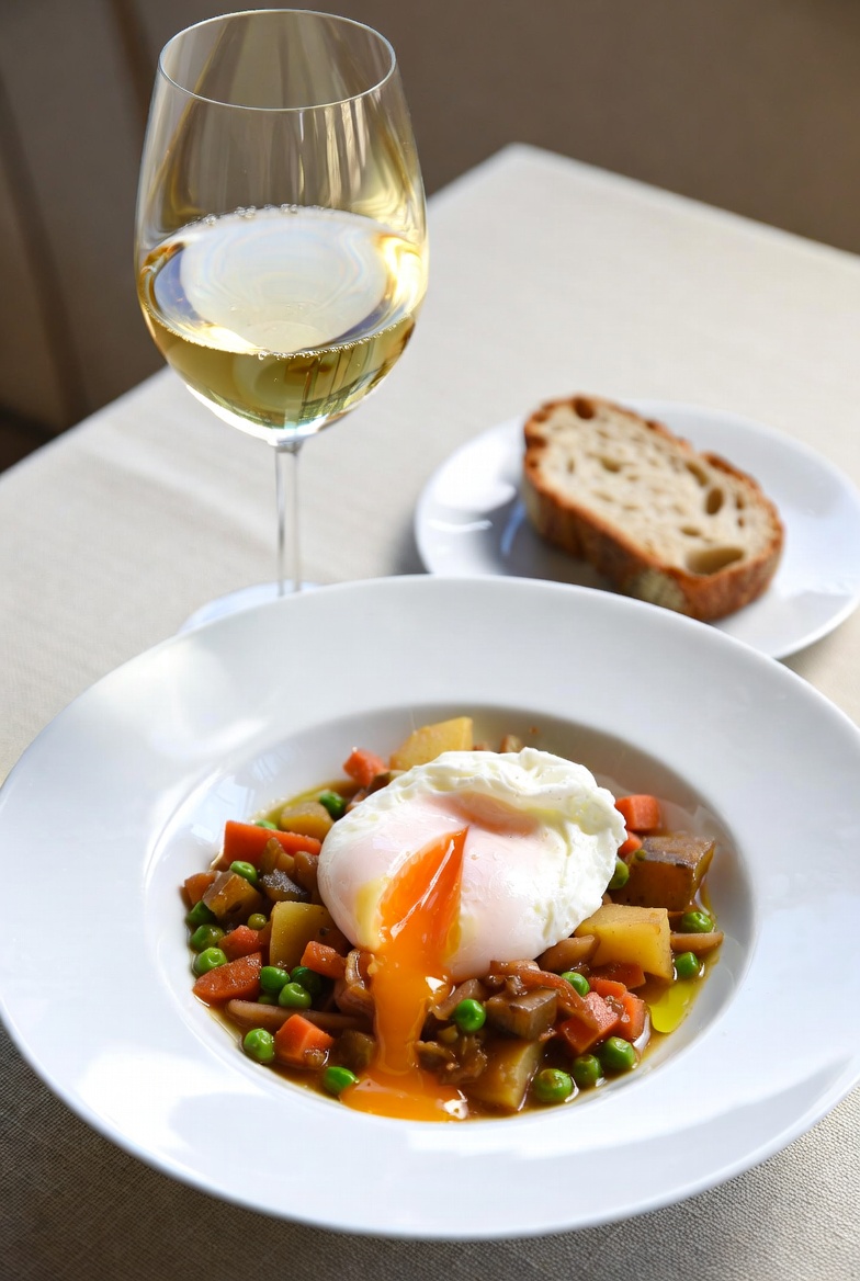 Plato de menestra riojana tradicional servido con huevo escalfado y vino blanco.