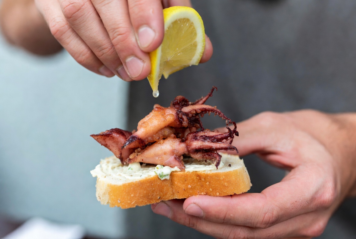 Manos colocando calamares fritos crujientes dentro de un panecillo para hacer un mini bocadillo