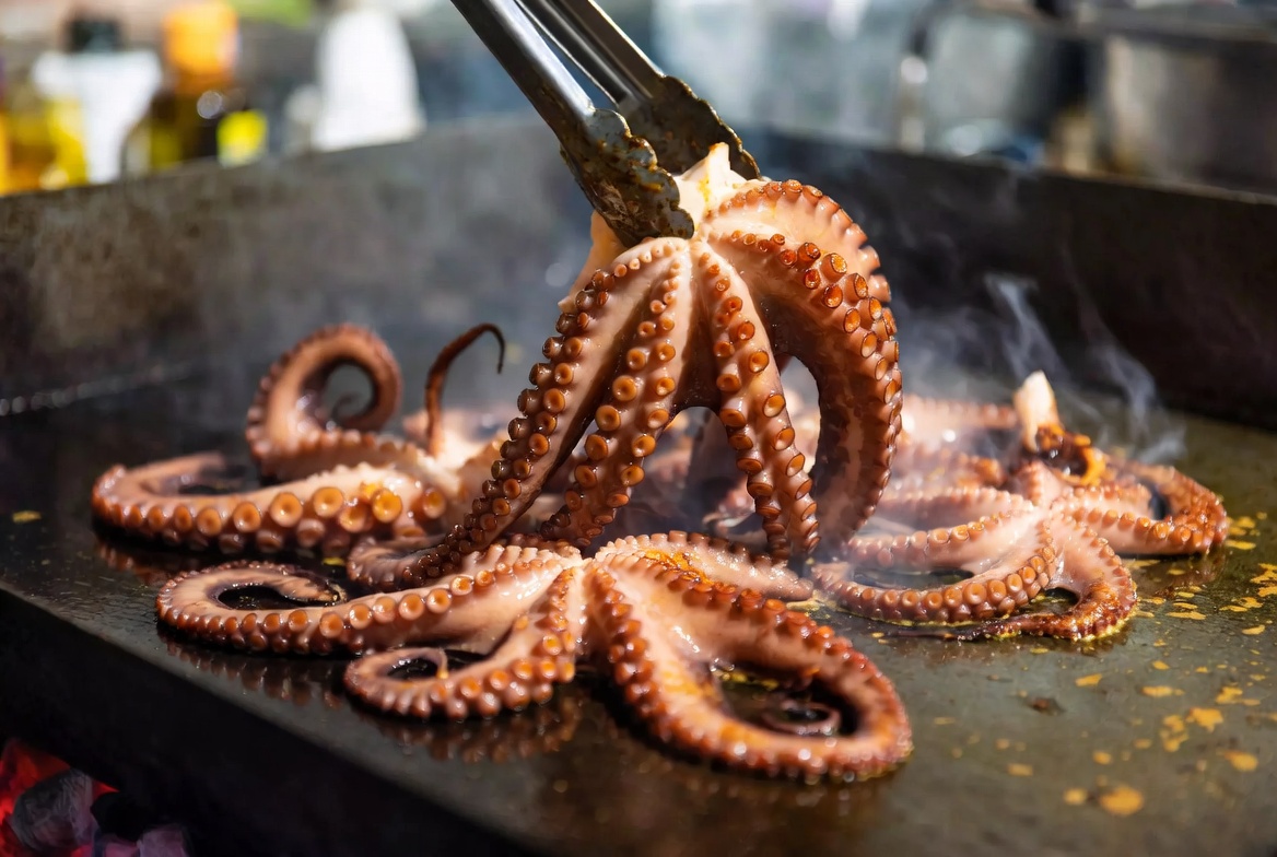 Tent&aacute;culos de pulpo sell&aacute;ndose y dor&aacute;ndose en una plancha a fuego vivo.