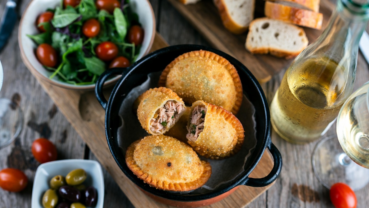 Mesa con empanadillas fr&iacute;as, ensalada, vino y acompa&ntilde;amientos para una comida al aire libre