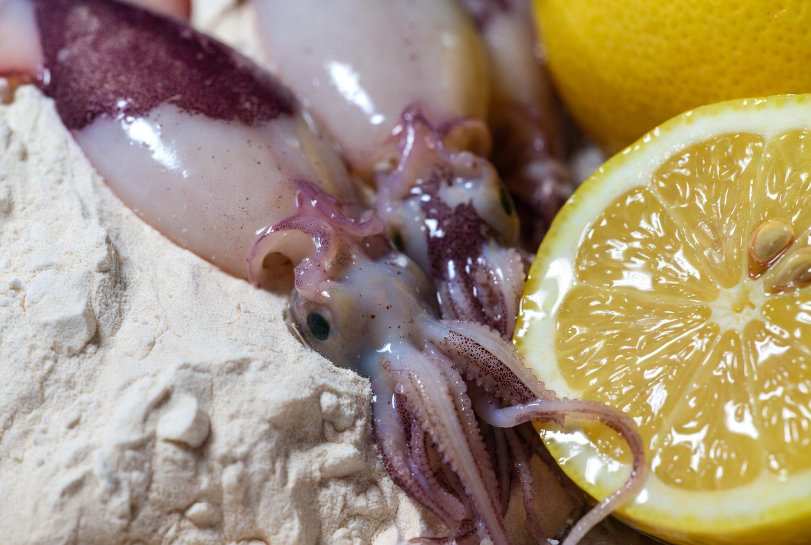 Ingredientes frescos para puntillitas fritas: calamar&iacute;n picudo, harina y lim&oacute;n sobre tabla de madera r&uacute;stica
