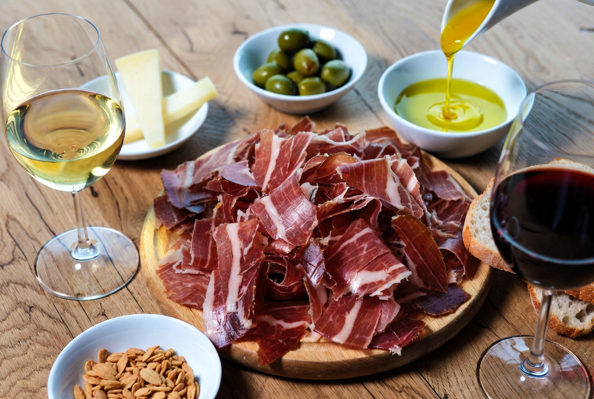 Tabla gourmet con lonchas de Jam&oacute;n Ib&eacute;rico de Bellota, queso, aceitunas y pan, ideal para compartir.